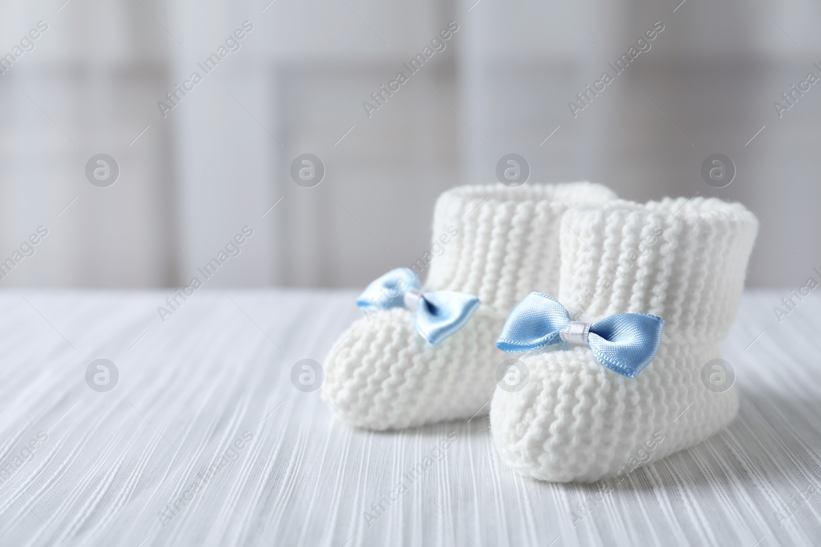 Photo of Handmade baby booties on plaid against blurred background. Space for text
