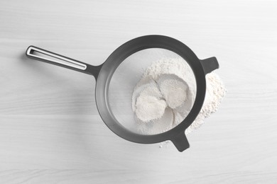 Photo of Sieve and flour on white wooden table, top view