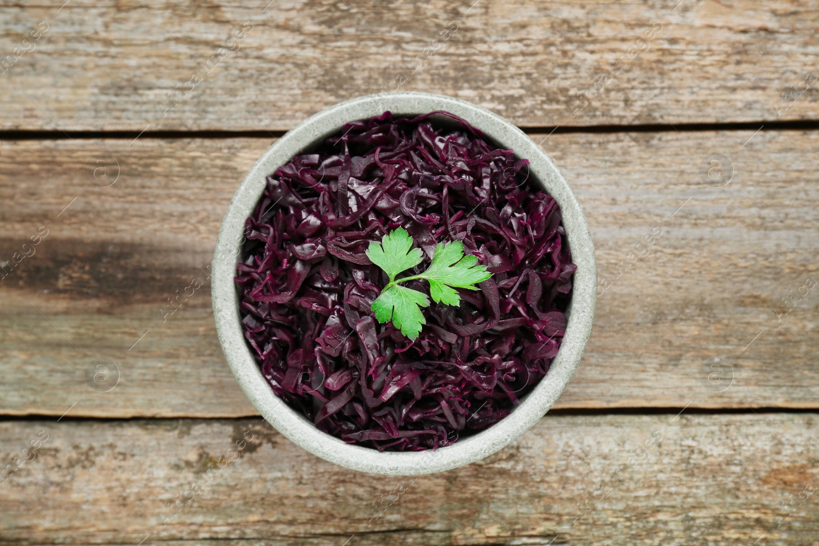 Photo of Tasty red cabbage sauerkraut with parsley on wooden table, top view