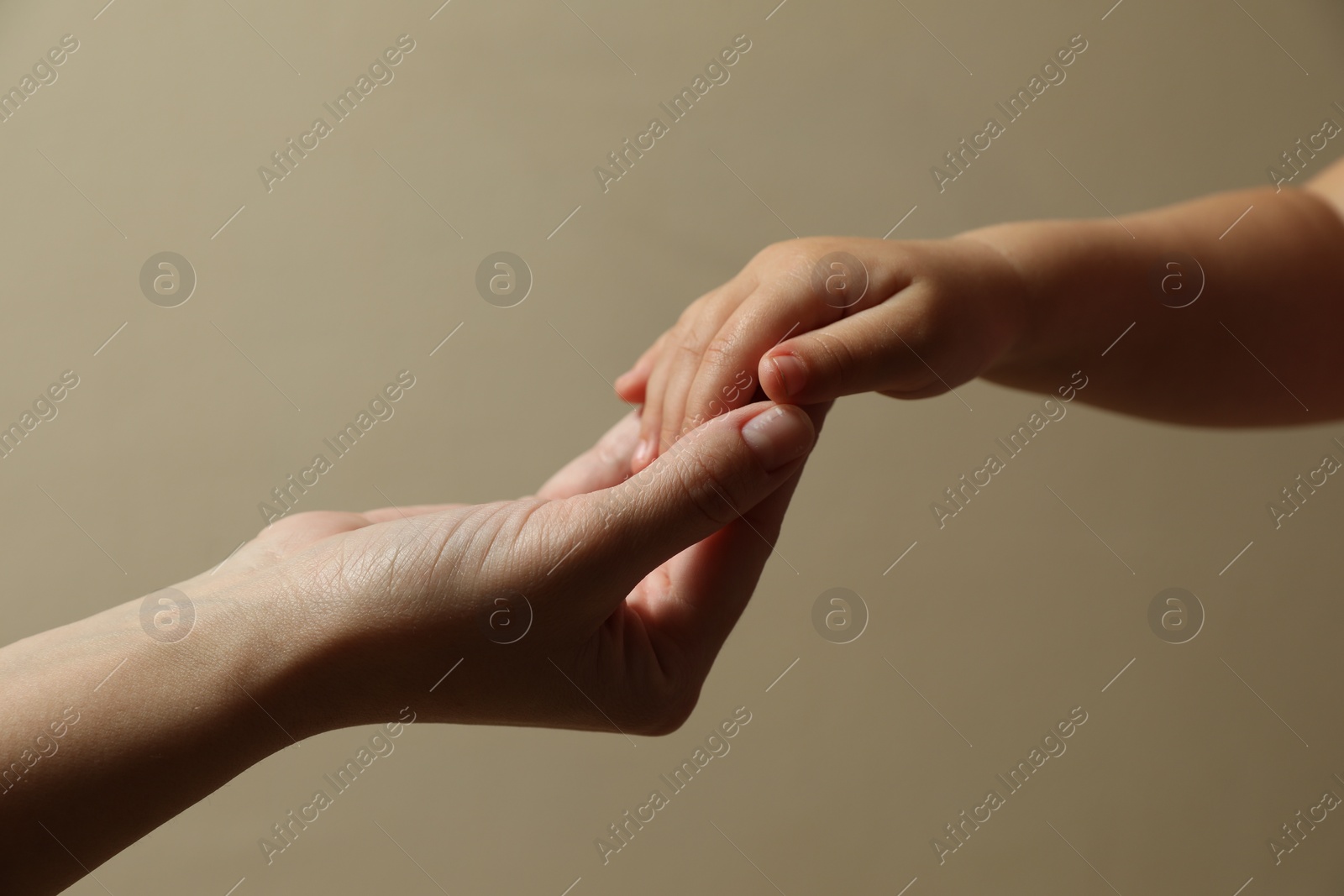 Photo of Mother and child holding hands on beige background, closeup