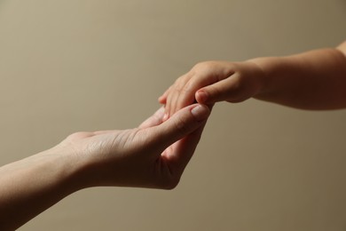 Mother and child holding hands on beige background, closeup