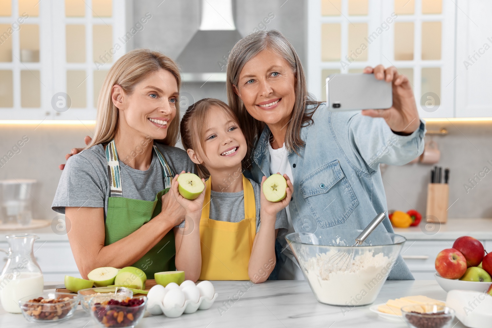 Photo of Three generations. Happy grandmother, her daughter and granddaughter taking selfie while cooking together in kitchen