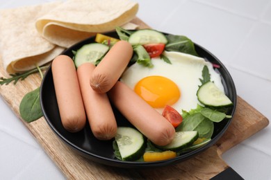 Delicious breakfast with boiled sausages and fried egg on white tiled table