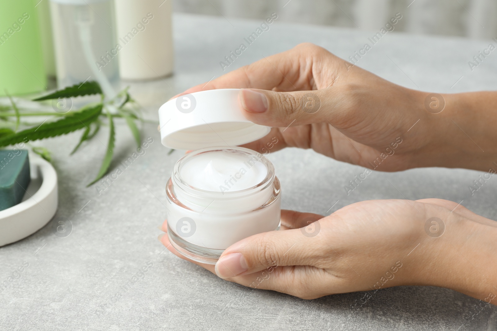 Photo of Woman holding jar of hemp cream at light table, closeup. Natural cosmetics