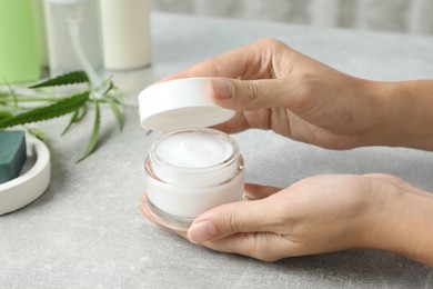 Woman holding jar of hemp cream at light table, closeup. Natural cosmetics