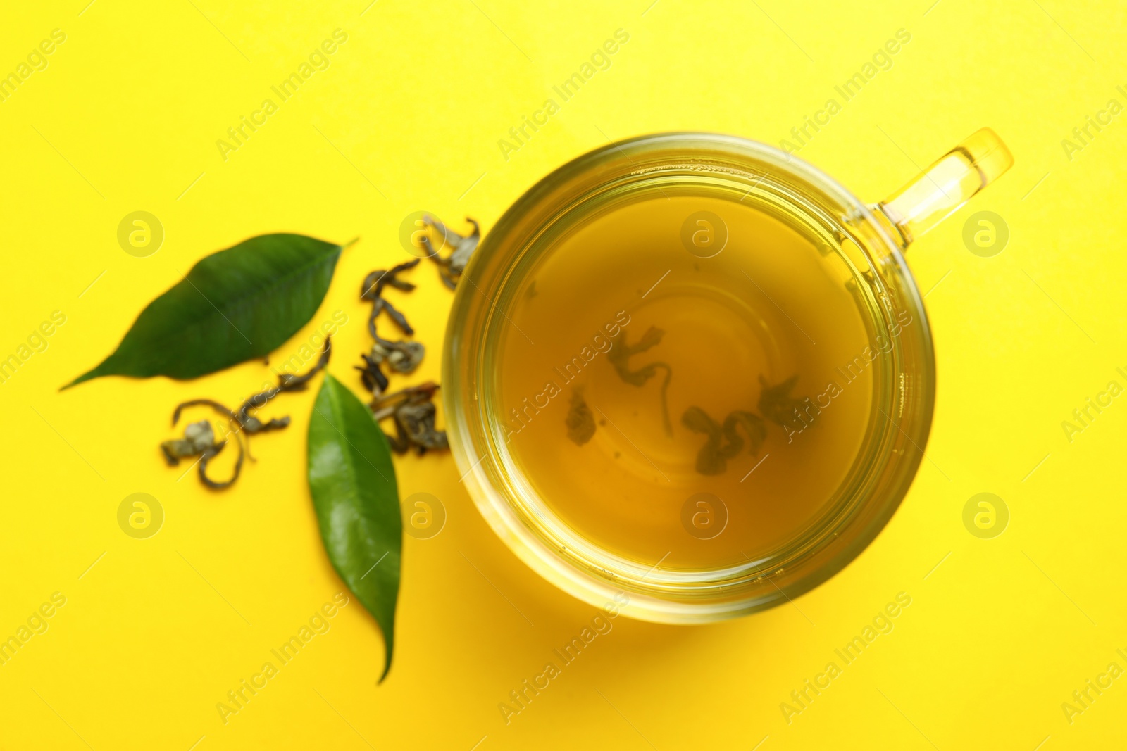 Photo of Cup of green tea and leaves on yellow background, flat lay