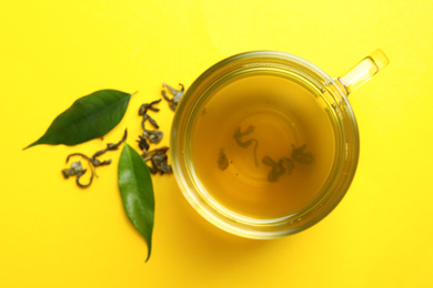 Photo of Cup of green tea and leaves on yellow background, flat lay