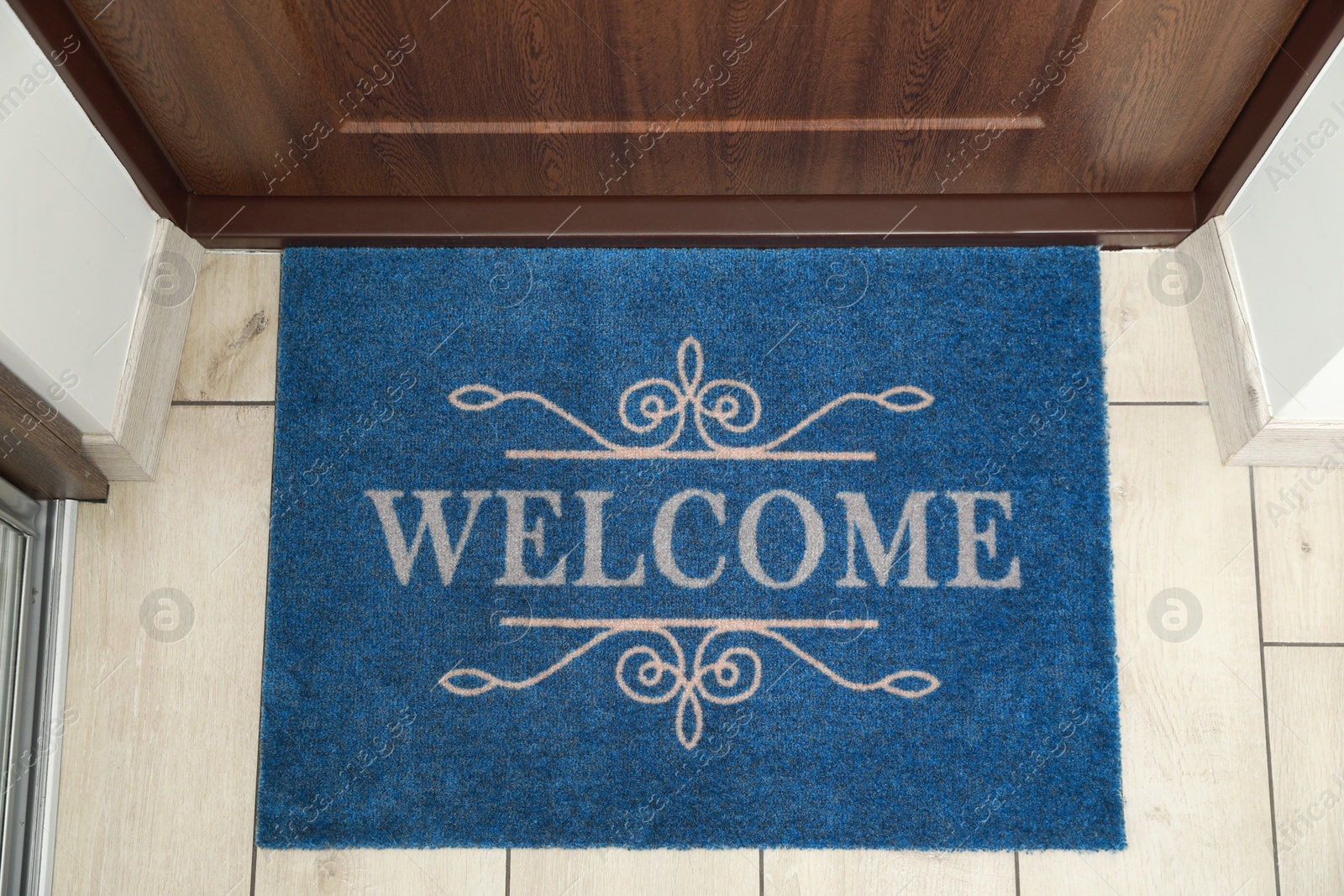 Photo of Beautiful blue doormat with word Welcome on floor near entrance, top view