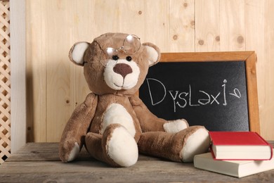 Photo of Teddy bear, small blackboard with word Dyslexia and books on wooden table
