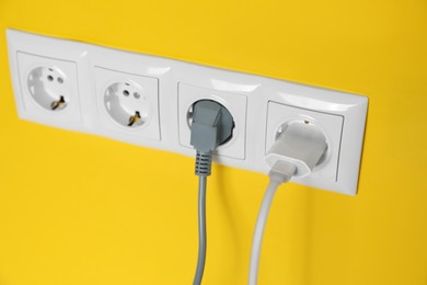 Power sockets with inserted plugs on yellow wall, closeup. Electrical supply