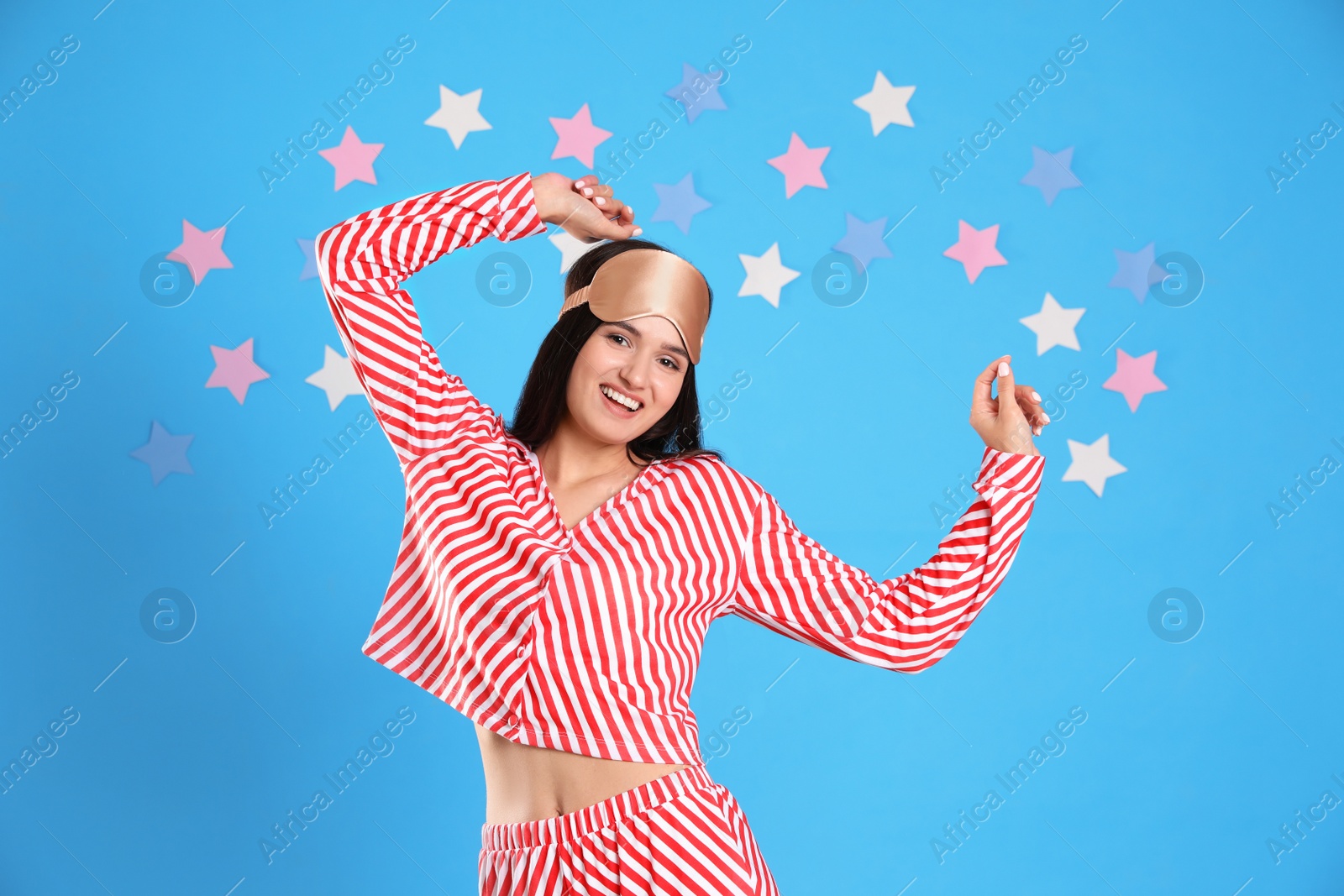 Photo of Beautiful woman wearing sleeping mask on light blue background. Bedtime