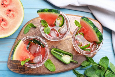 Photo of Glasses of spicy cocktail with jalapeno and mint on light blue wooden table, flat lay