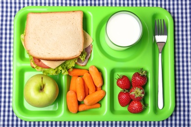 Serving tray with healthy food on tablecloth, top view. School lunch