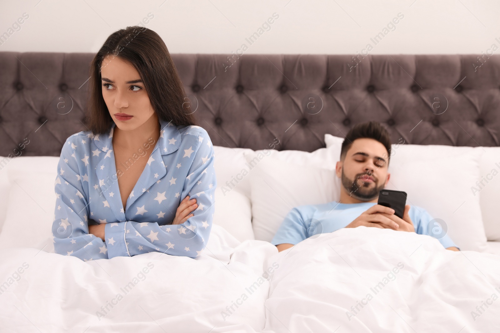 Photo of Young man preferring smartphone over his girlfriend in bed at home