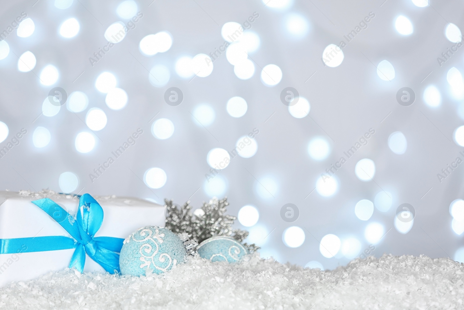 Photo of Christmas decoration and gift box on snow against blurred background, space for text