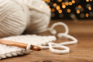 Photo of Knitting and crochet hook on wooden table against blurred lights, closeup. Space for text