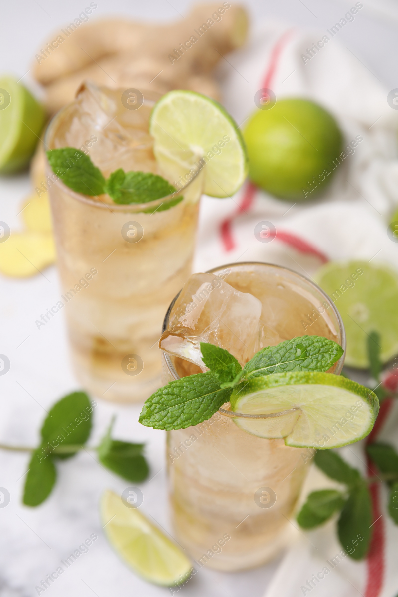 Photo of Glasses of tasty ginger ale with ice cubes, lime slices and mint on blurred background
