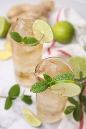Glasses of tasty ginger ale with ice cubes, lime slices and mint on blurred background
