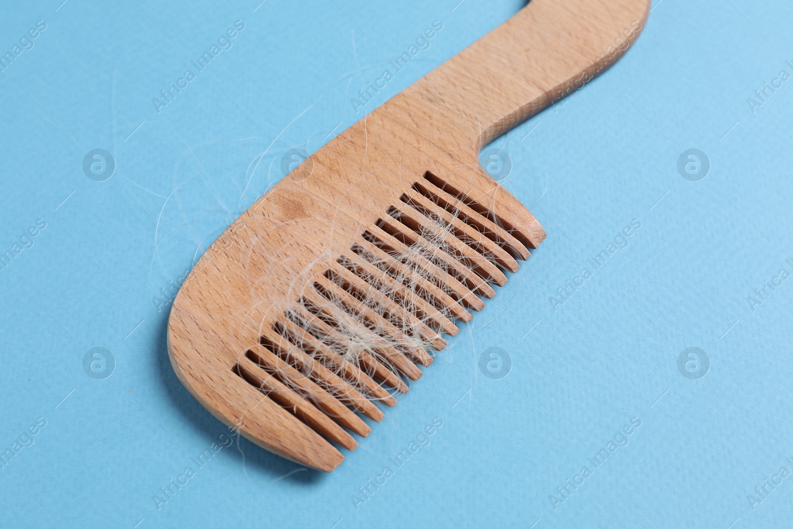 Photo of Wooden comb with lost hair on light blue background