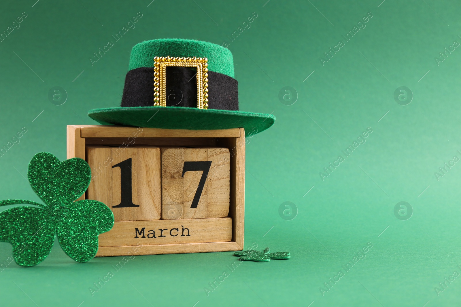 Photo of St. Patrick's day - 17th of March. Wooden block calendar, leprechaun hat and decorative clover leaves on green background. Space for text