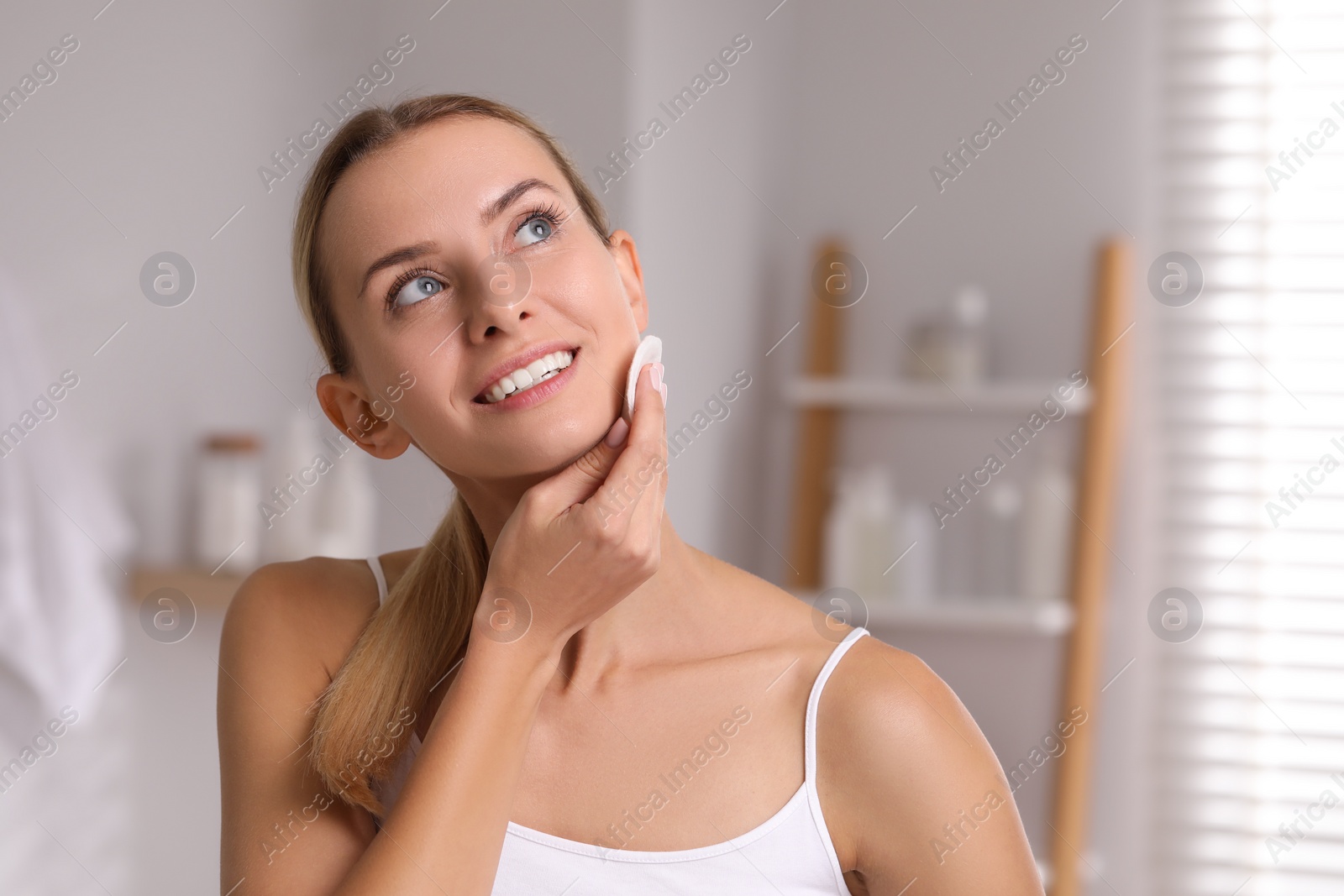 Photo of Smiling woman removing makeup with cotton pad indoors