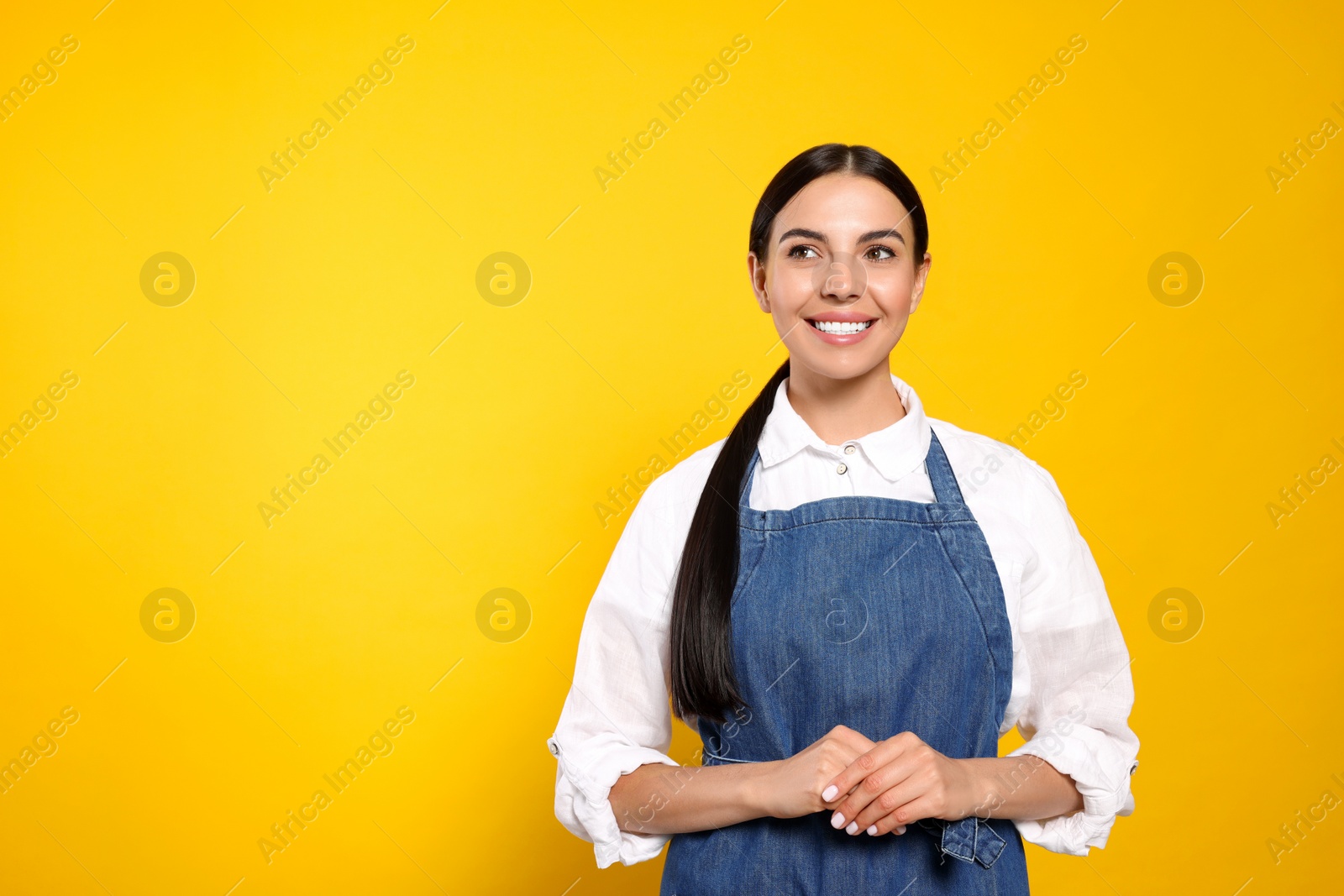 Photo of Young woman in blue jeans apron on yellow background, space for text