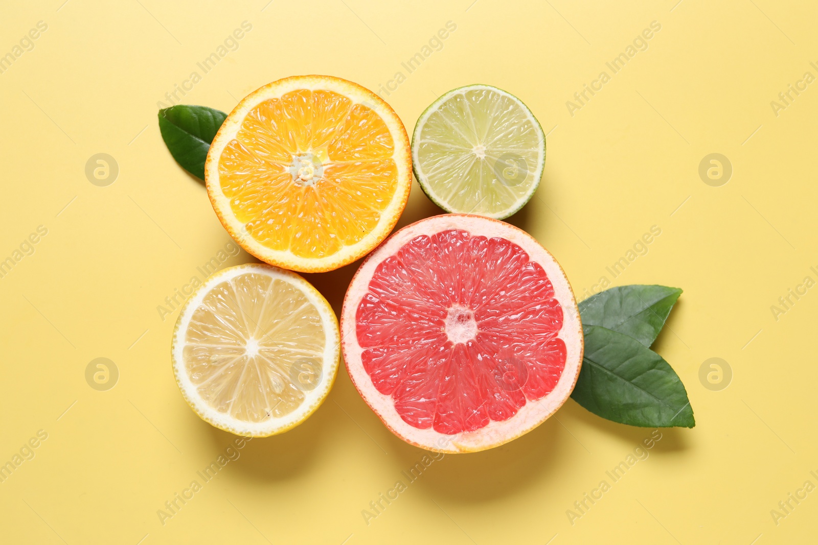 Photo of Different cut citrus fruits and leaves on yellow table, flat lay