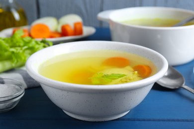 Delicious chicken bouillon with carrot and celery on blue wooden table, closeup