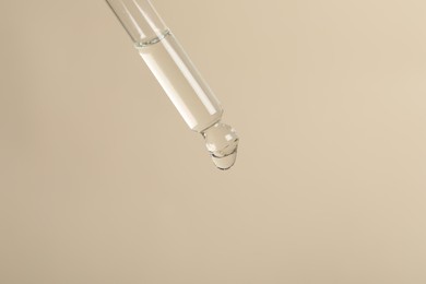 Photo of Dripping cosmetic serum from pipette on beige background, space for text