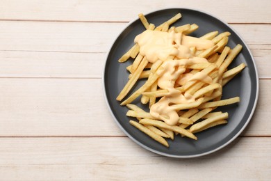 Photo of Delicious french fries with cheese sauce on wooden table, top view. Space for text