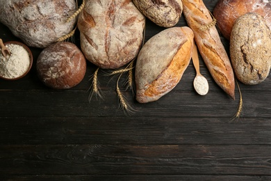 Photo of Different kinds of fresh bread on black wooden table, flat lay. Space for text