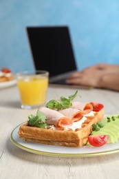 Photo of Woman working with laptop at wooden table during breakfast