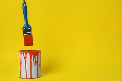 Photo of Can of orange paint and brush on yellow background. Space for text