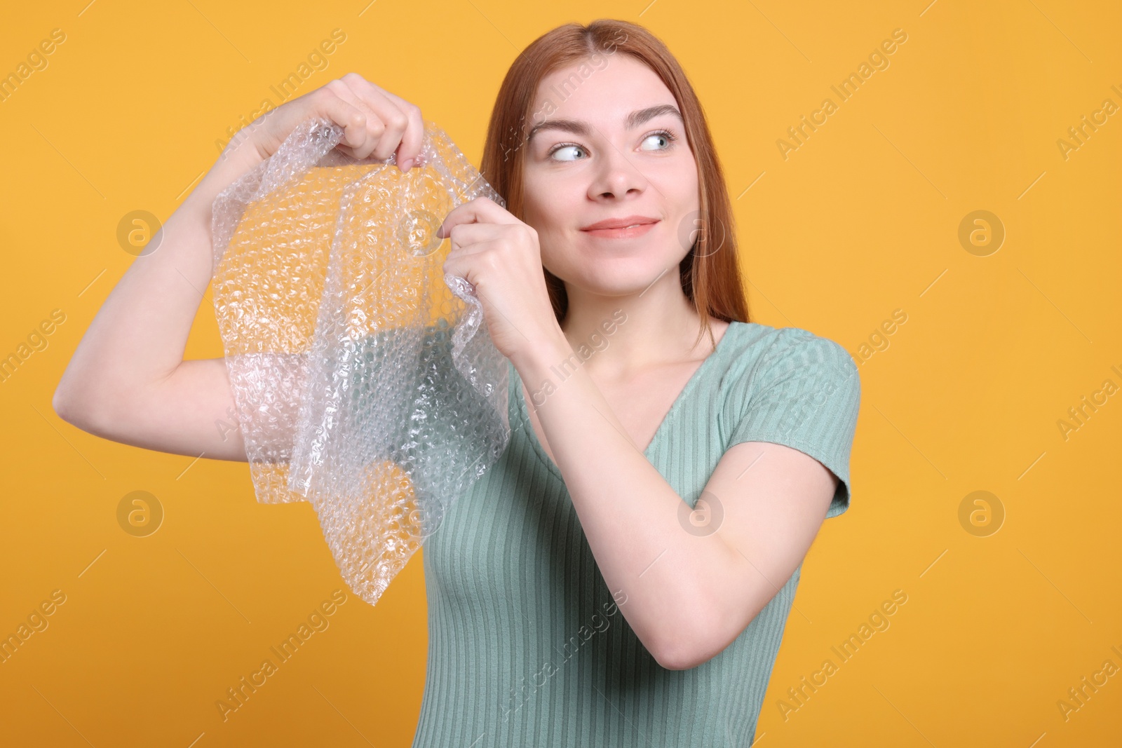 Photo of Woman popping bubble wrap on yellow background. Stress relief