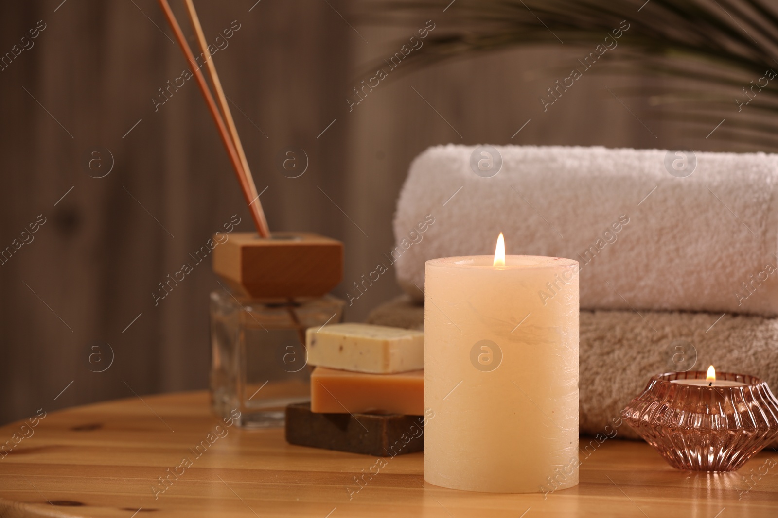 Photo of Spa composition. Burning candles, towels, soap and reed air freshener on wooden table, closeup