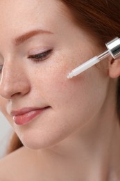 Photo of Beautiful woman with freckles applying cosmetic serum onto her face, closeup