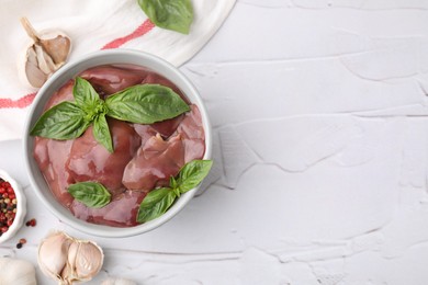 Bowl with raw chicken liver, garlic, peppercorns and basil on white textured table, flat lay. Space for text