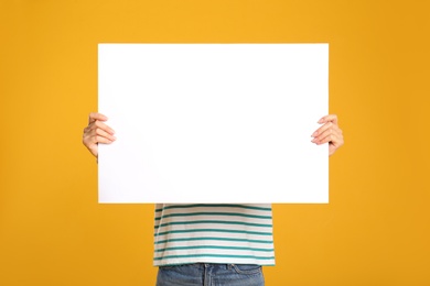 Woman holding white blank poster on yellow background. Mockup for design