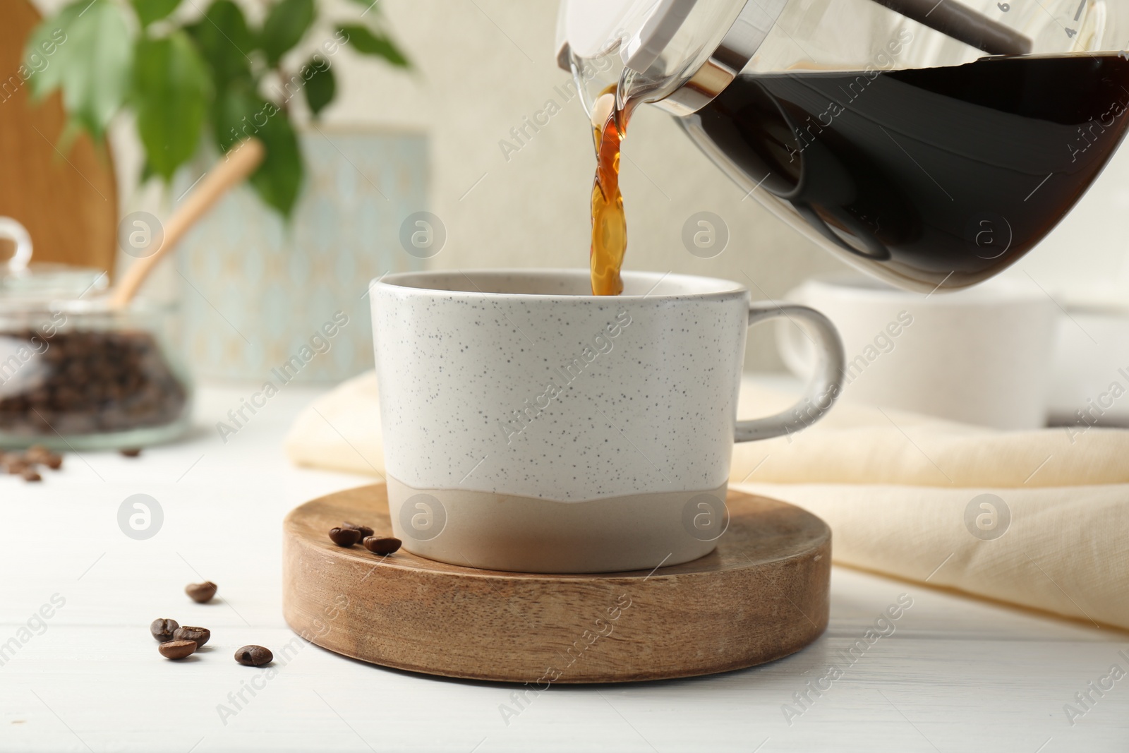 Photo of Pouring coffee into cup at white wooden table, closeup