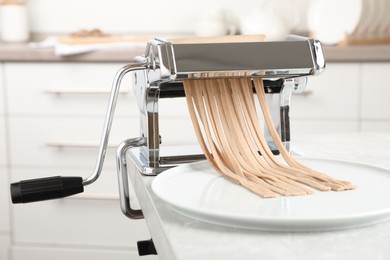 Photo of Preparing soba (buckwheat noodles) with pasta maker machine at table in kitchen