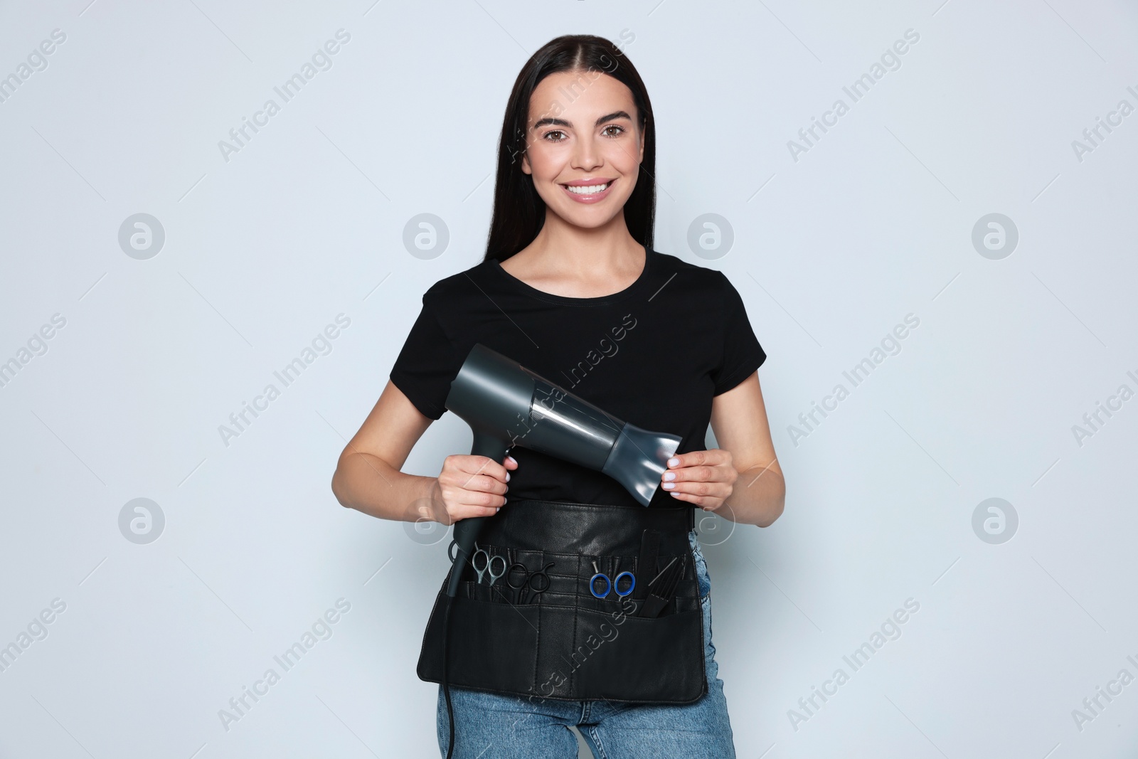 Photo of Portrait of happy hairdresser with hairdryer and professional tools on light background