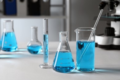 Different laboratory glassware with light blue liquid on table