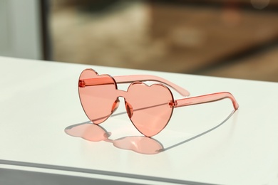 Photo of Stylish heart shaped sunglasses on table against blurred background. Space for text