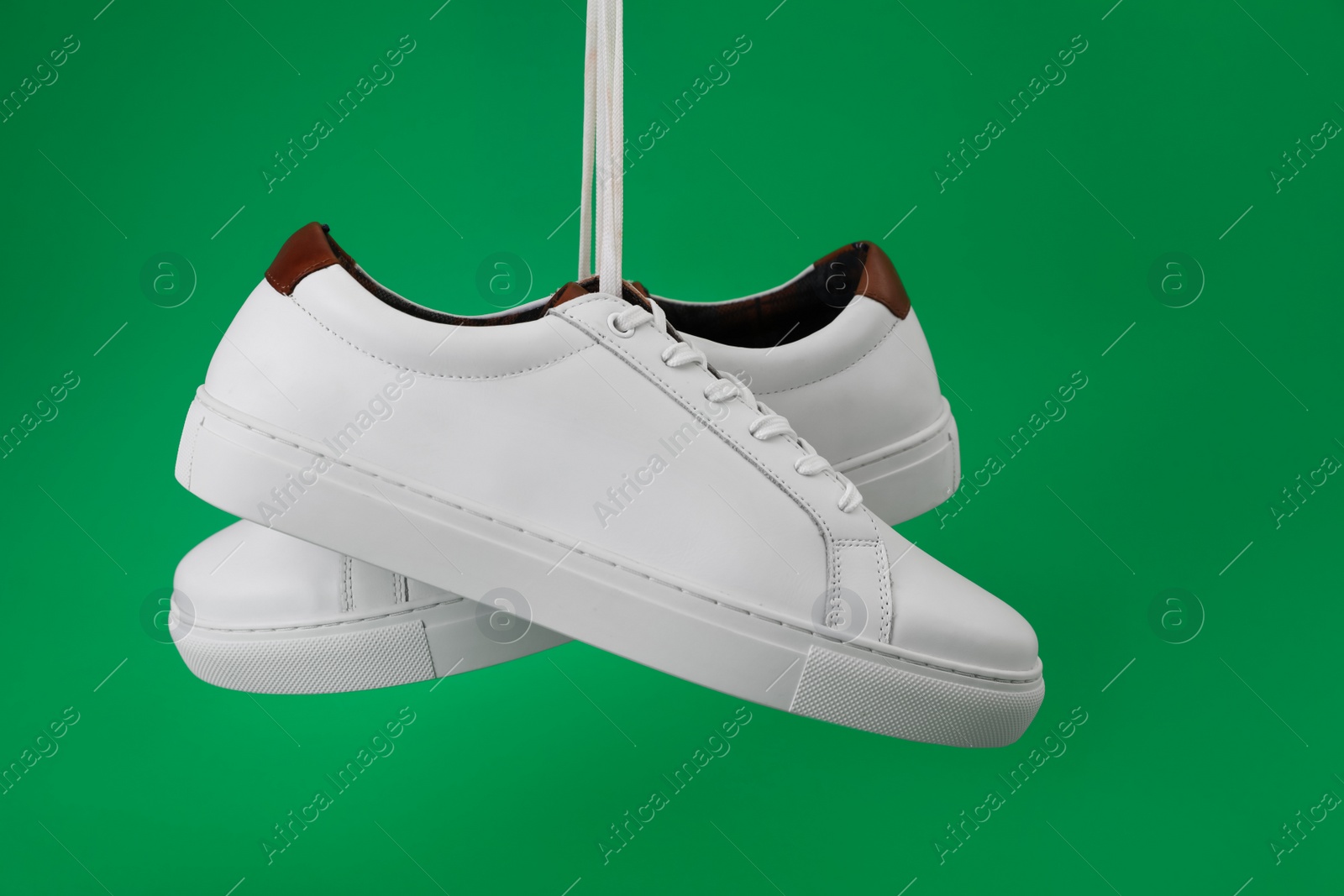 Photo of Pair of stylish sports shoes hanging on green background