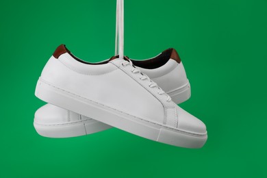 Pair of stylish sports shoes hanging on green background