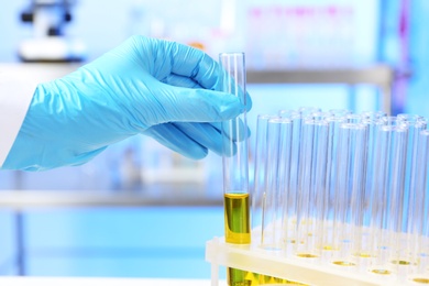 Photo of Laboratory assistant taking test tube with urine sample for analysis from holder on table, closeup