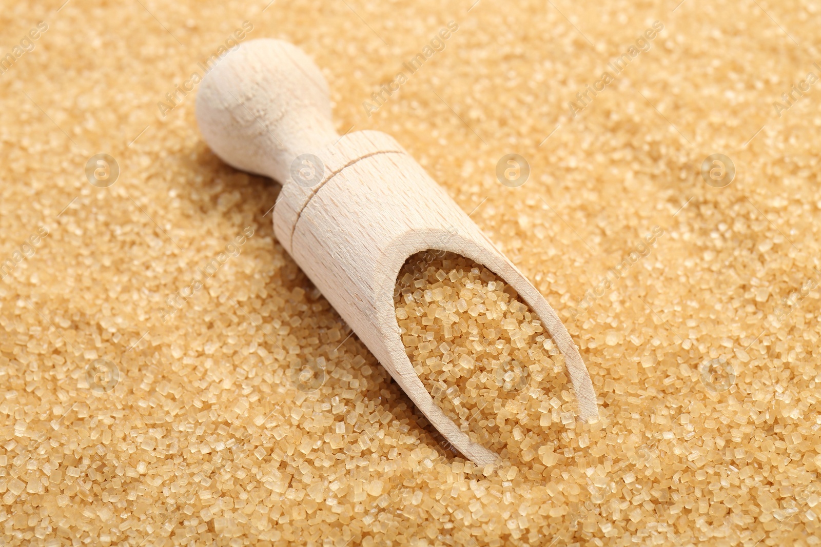 Photo of Wooden scoop on granulated brown sugar, closeup view