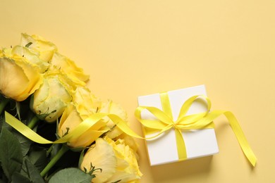 Beautiful bouquet of yellow roses and gift box on beige background, flat lay. Space for text