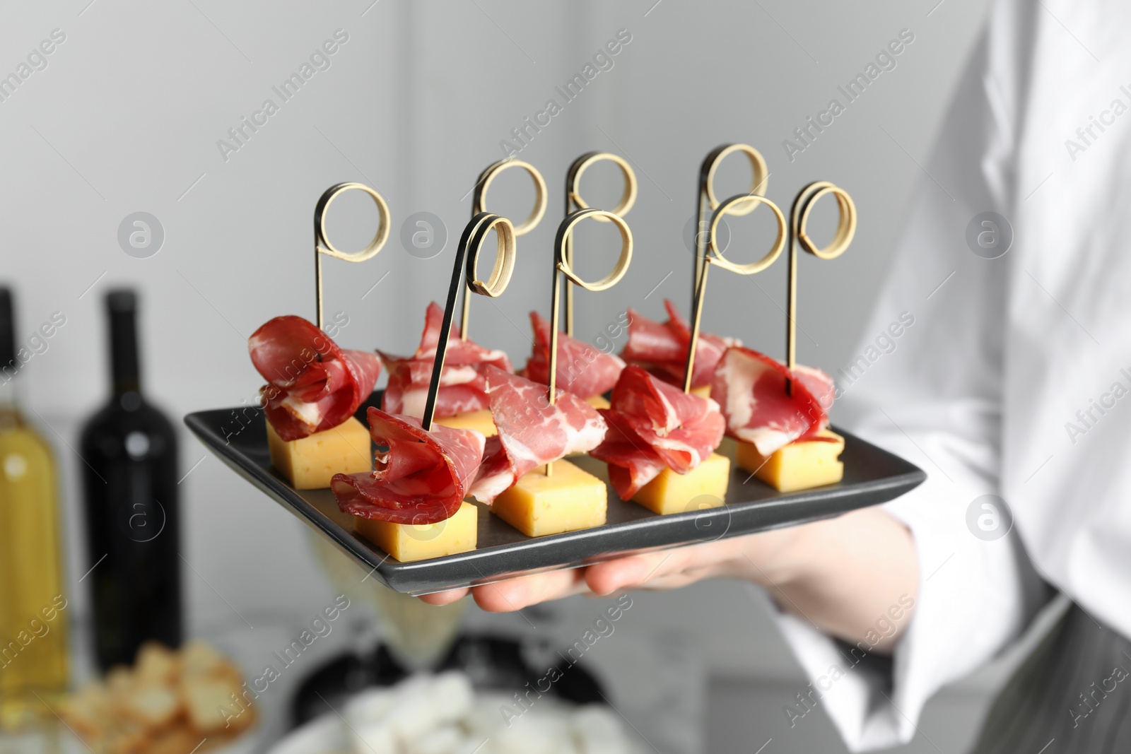 Photo of Woman holding plate of tasty canapes with ham and cheese indoors, closeup