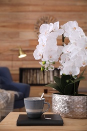 Photo of Beautiful white orchids and cup of tea on wooden table in living room. Interior design
